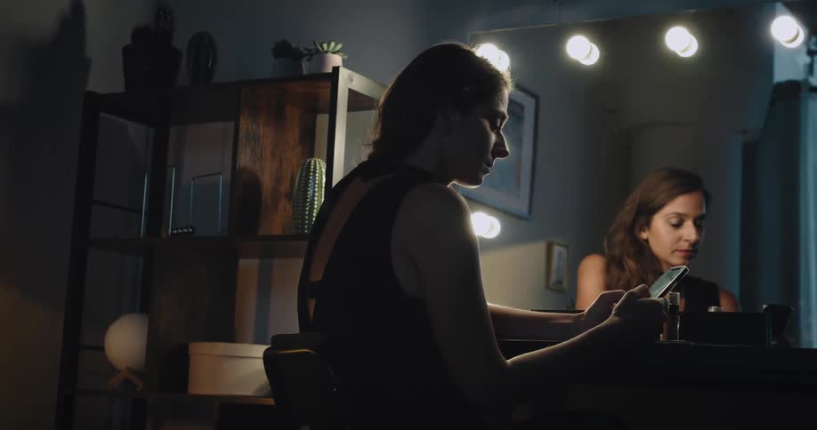 A woman sitting in front of a mirror texting on her cell phone