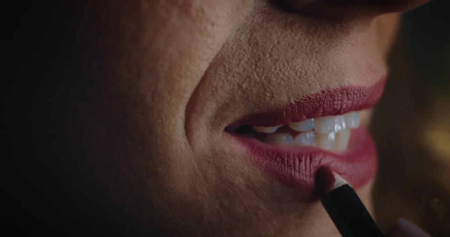 Woman applying red lip liner pencil to lips with red lipstick already applied smiles