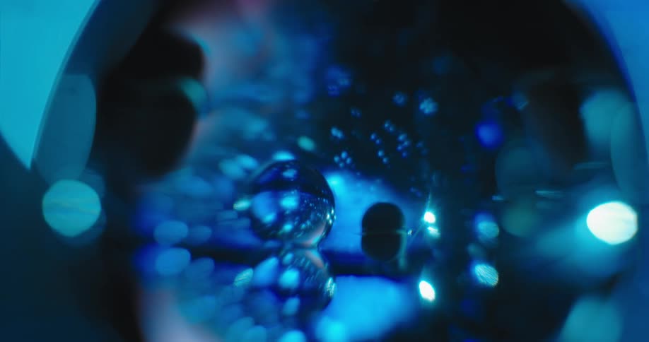 Blue light glows in the distance and reflects on clear orbs floating in the darkness