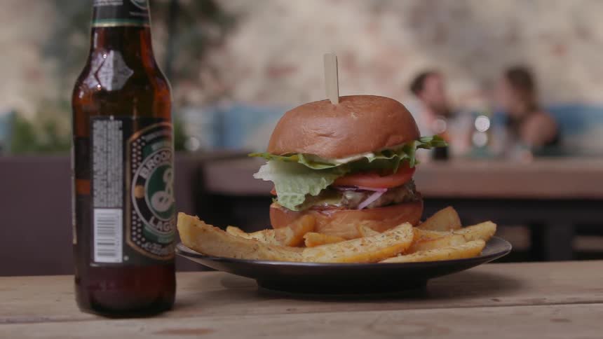 A waiter is setting a hamburger down next to a beer on a table