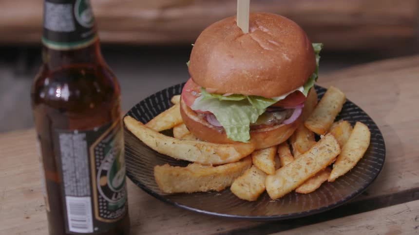 A person places a burger on a table next to a bottle of beer