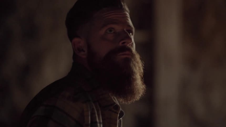 A man with a long beard slowly gets up