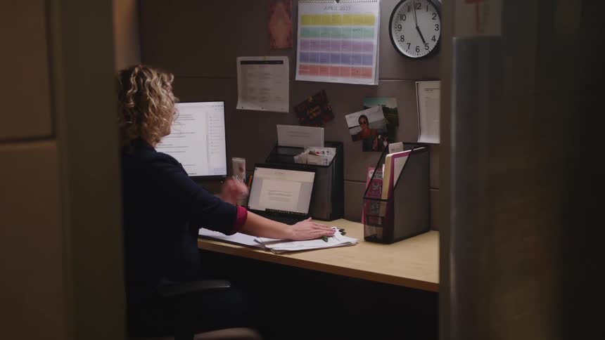 Woman working at desk in office looks at wall clock and leaves since it is quitting time