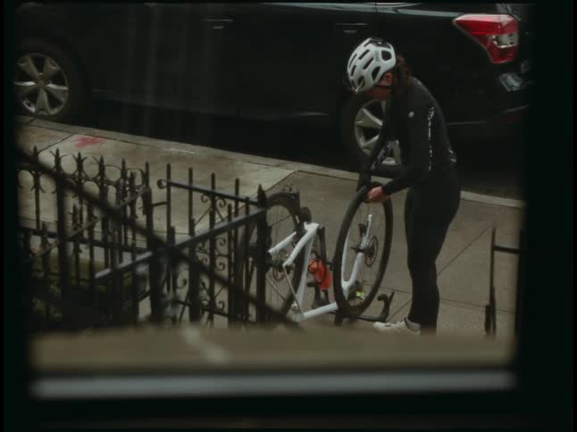Cyclists works on bicycle tire while standing on sidewalk near ironwork fence