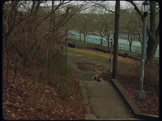 A bicyclist riding through a city park with a tennis court in the background