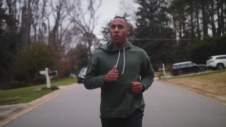 A man wearing a hoodie is jogging on a neighborhood street