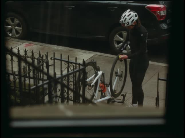 A woman changes a bicycle wheel on her front stoop