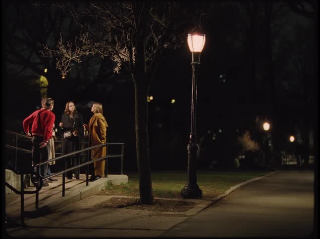 A group of four friends talk near a street at night while drinking wine from the bottle