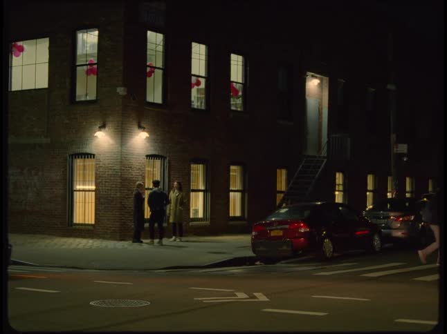 A group of friends chat outside an apartment building as vehicles drive by