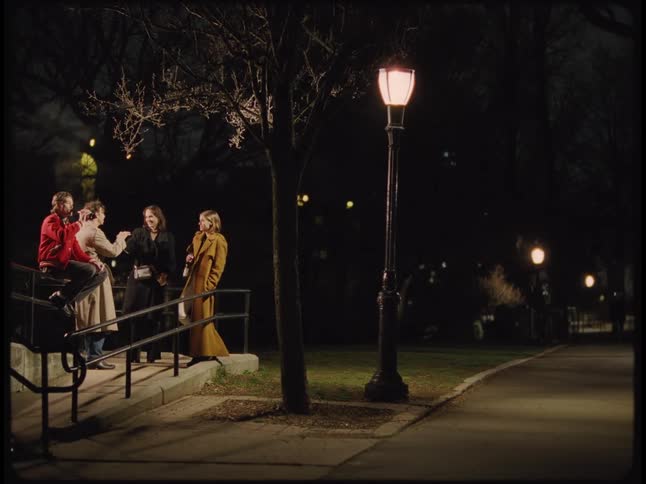 A group of people stand outside at night socializing as a bicyclist passes by