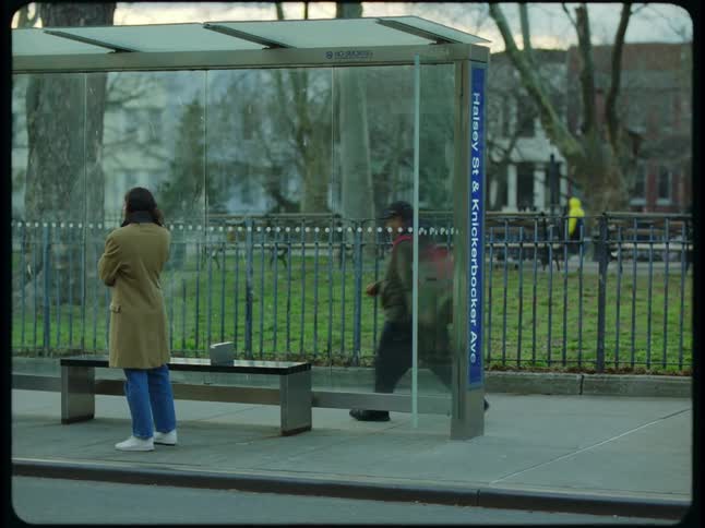 Young girl with long red hair at city bus stop talking on phone paces for a moment and sits on bench
