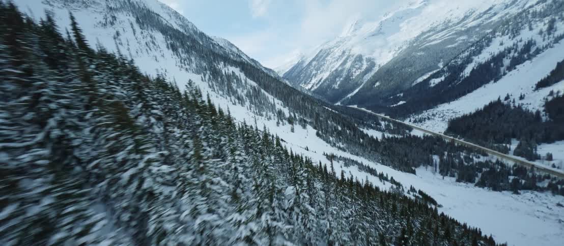 An aerial camera sweeps across a winter valley full of trees between snowy mountain peaks
