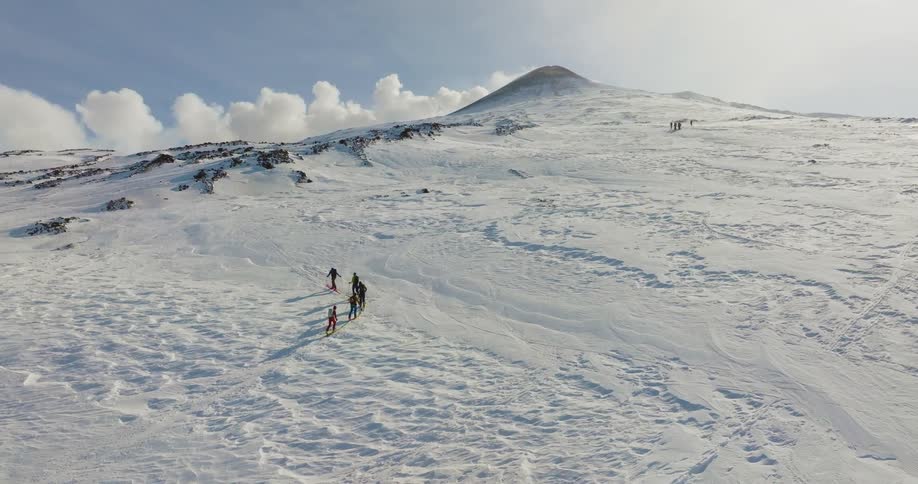 Two groups of skiers cast shadows on the snow as they move up mountain slope