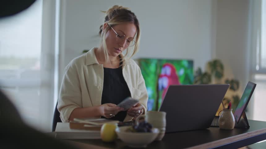 Woman sits at table flipping through small notepad and using laptop