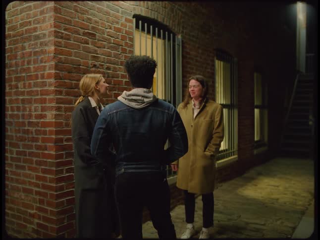 A man and a woman are standing outside next to a building talking and another woman walks down the stairs and speaks to them and they all walk away