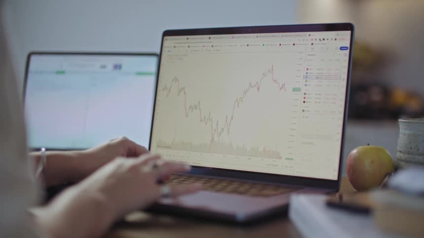 Woman sits at dining table working with graphs on her laptop