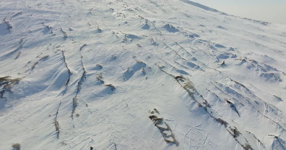 Aerial view of snowy mountain slope and mountain peak while the sun shining