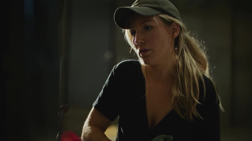 A woman wearing a black tshirt and grey cap using tools to work on equipment