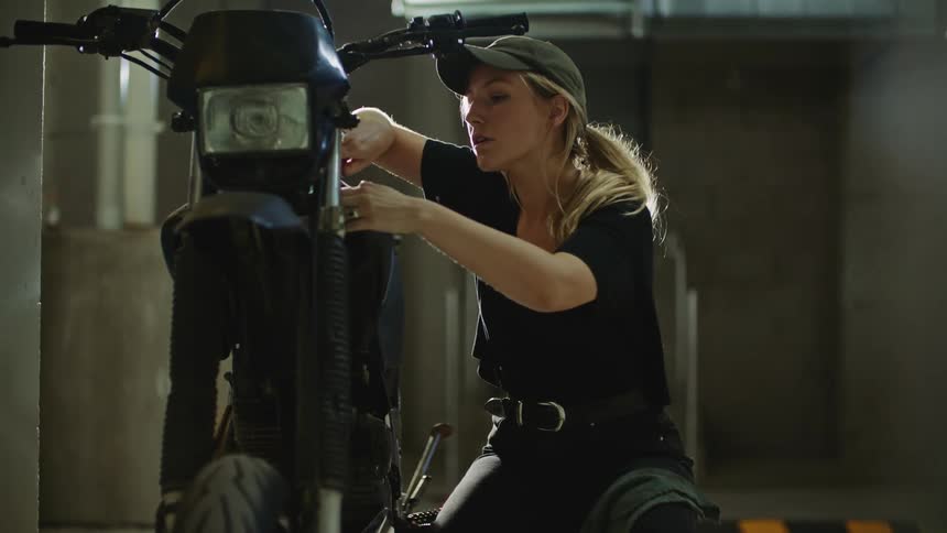 A woman sitting next to a motorcycle suing tools to work on it