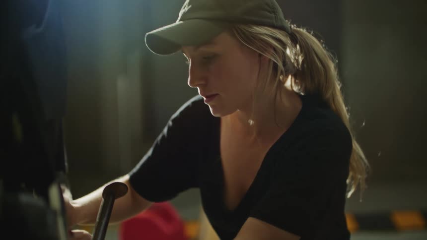 Blonde woman working on a broken stationary bike using a wrench