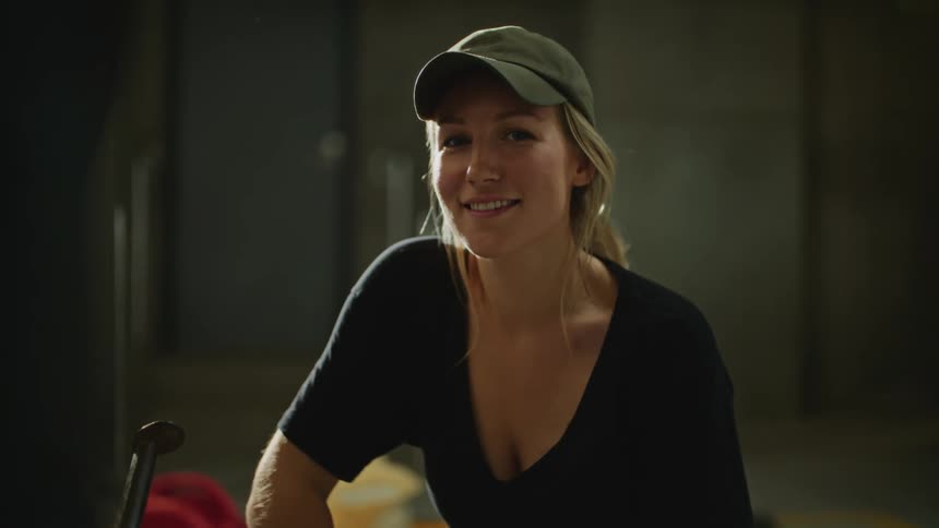 Young blonde woman sitting next to stationary bike in a gym and smiling at the camera