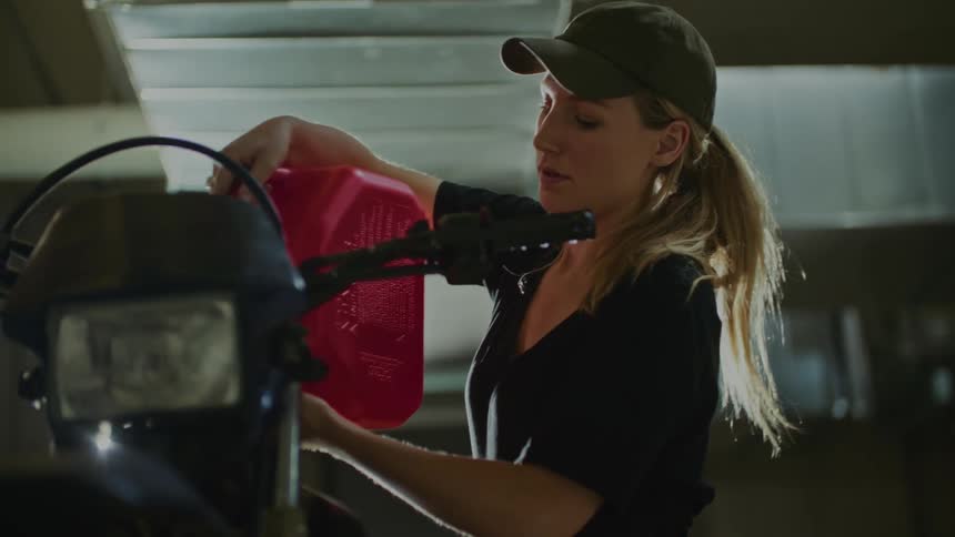A woman uses a gas can to pour gas in her motorcycle
