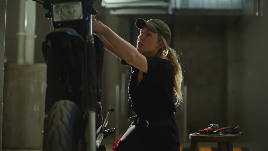 Young blonde mechanic woman working on motorcycle with tools in a garage