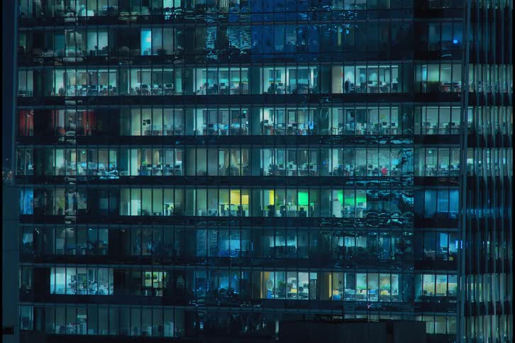 People move around the office building with blinking and flickering window lights