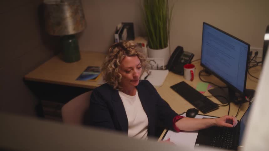 A woman sits bored at her desk closes her laptop and leaves