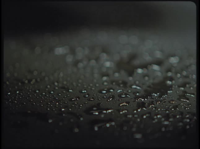 Water droplets fall onto a black surface