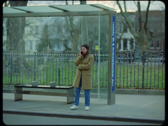 A woman walks on a neighborhood street near a bus stop as she talks on her phone
