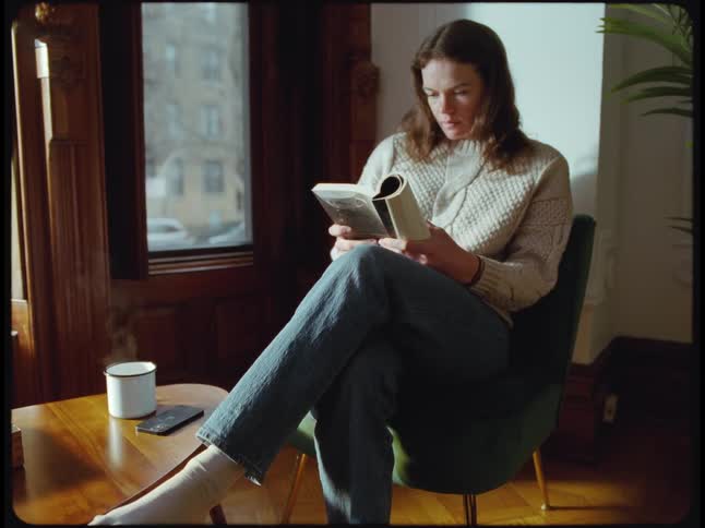 A woman checks her phone after sitting down with a book and drink