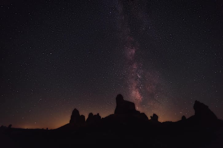 The beautiful purple star filled night sky is being shown behind a silhouette of large rocks