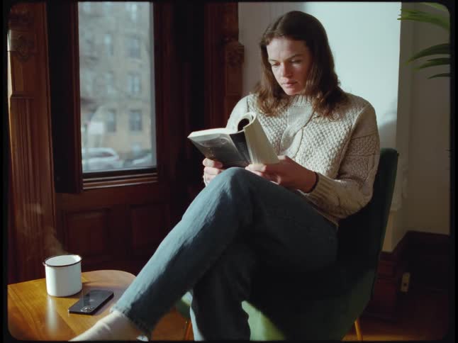 A woman is sitting indoors and reading a book