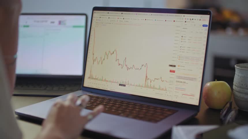 A womans arm is showing using a trackpad mouse to interact with stock information on the computer screen