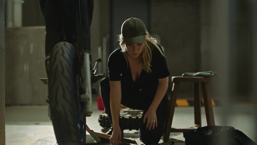 Woman half kneels while working on motorcycle