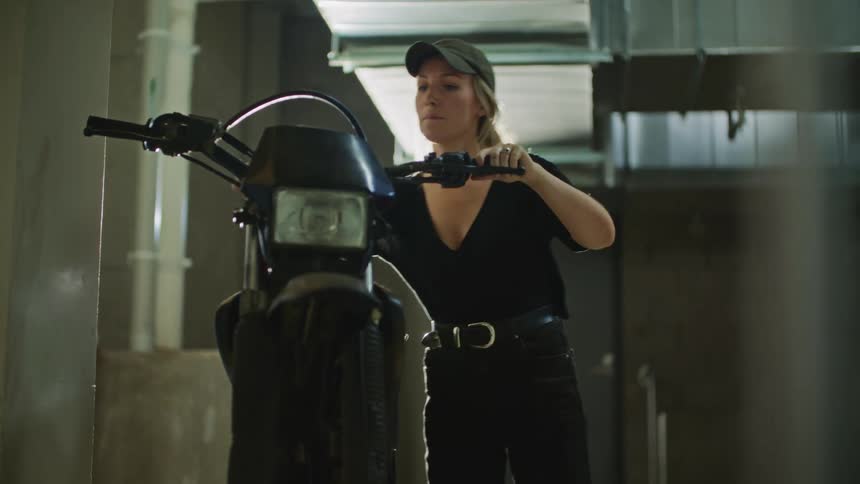 Blonde woman with black shirt and jeans cleans and checks dirt bike