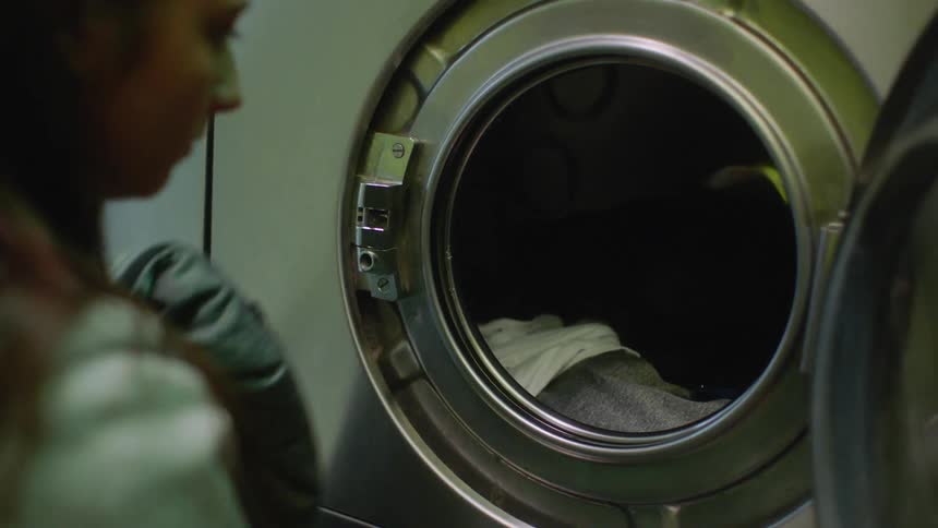 A young woman is adding clothes to a washing machine in a laundromat
