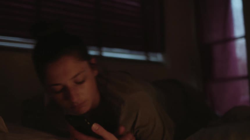 A young woman scrolling on a phone in bed and rolling over