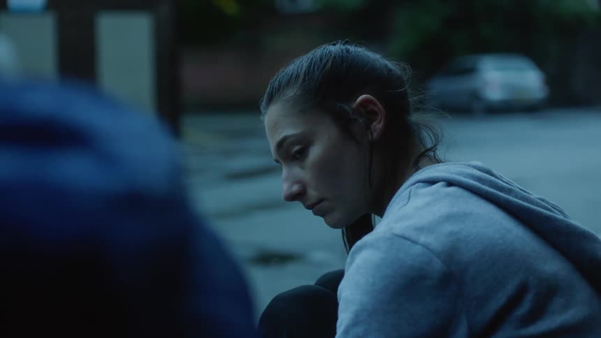 A teenage girl looks sad as she talks to another person on a neighborhood street