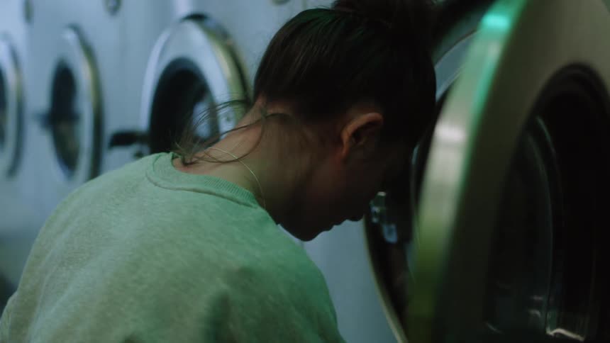 Woman with gray sweater and necklace loads washer with clothes in laundry shop