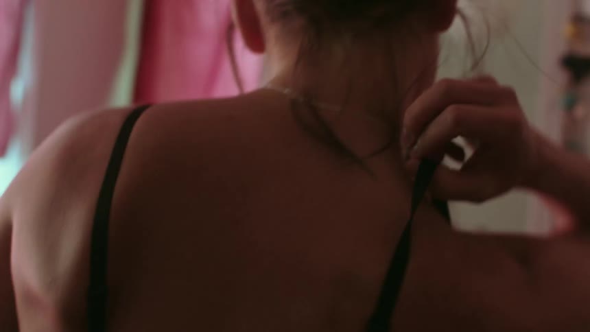 Woman puts on bra and looks at herself in the mirror