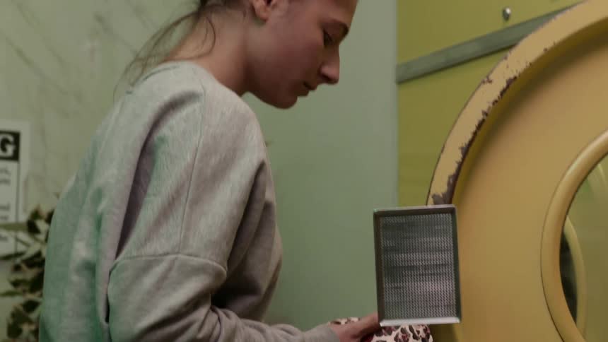 Woman with gray sweater and black pants takes bra from washing machine in laundry shop