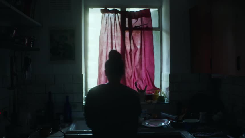 Woman silhouetted against the window washes dishes in the kitchen