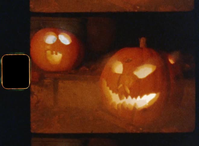 Super 8mm film stock of two carved pumpkins glowing in the darkness due to burning candles and fog on a misty fall night on October 31st in the backyard of a haunted old house
