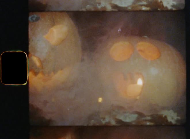 2 carved pumpkins with angry and scared facial expressions and evil smiles glowing and smoking on a misty autumn night lit up by creepy flickering flashing lights on 8mm footage with vintage film burn