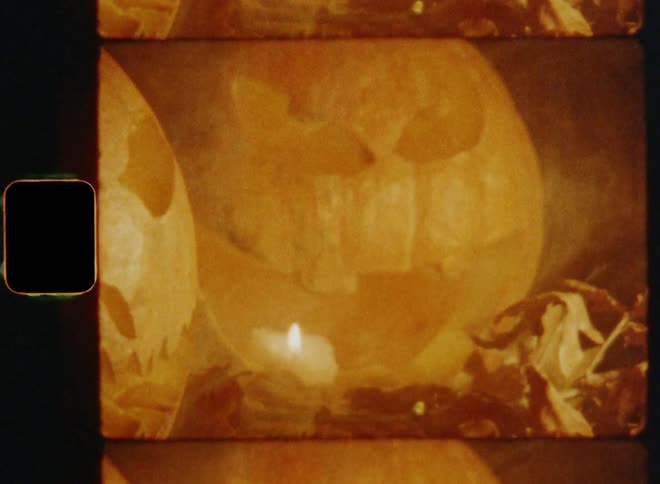 Vintage Super-8mm film footage of two evil and creepy looking steaming Halloween pumpkins surrounded by oak leaves outdoors at night as the smoke of the burning candles rises into the dark night sky on October 31st