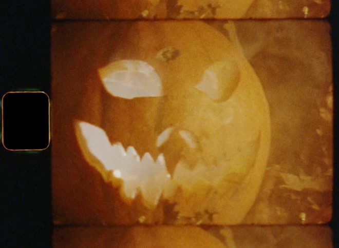Smoke fills the air as a carved pumpkin jack o lantern glows in the darkness underneath an oak tree with dead brown leaves on branches and twigs during the dark nighttime on Halloween evening celebrating all hallows eve on 31st October