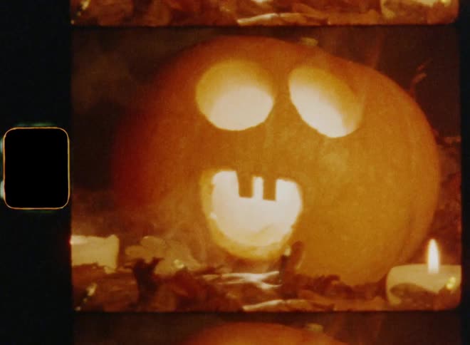 Orange carved Halloween pumpkin jack o lantern with shocked and surprised facial expression and a wide-open mouth that is glowing and smoking surrounded by burning candles and dead brown oak leaves on nostalgic 8mm film