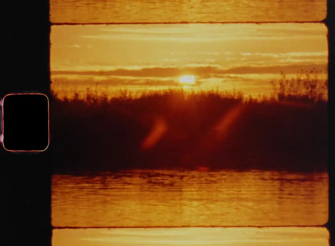 The sun shines brightly as it disappears behind the clouds at the horizon during a beautiful sunset or sunrise with bright orange sunlight shining onto and reflecting on the rippling surface of the water or lake